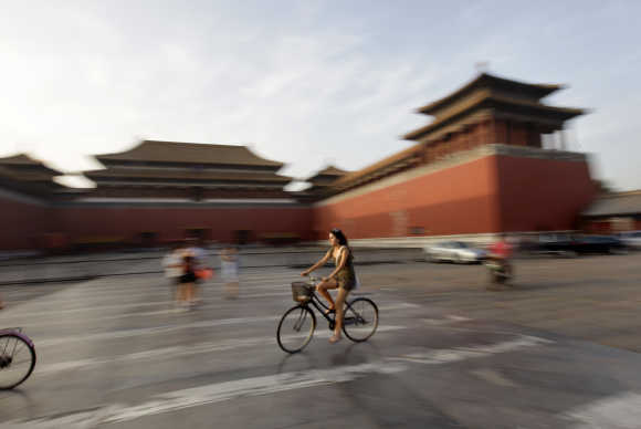 A foreign visitor rides a bicycle past Wumen Gate at the Forbidden City in Beijing.