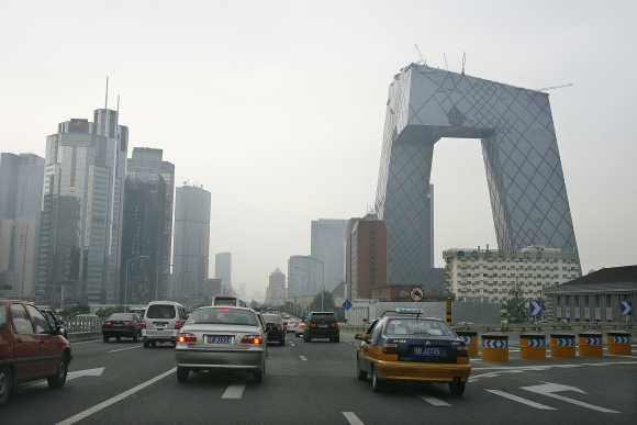 Vehicles pass a major thoroughfare towards the China Central Television headquarters, right, in Beijing.
