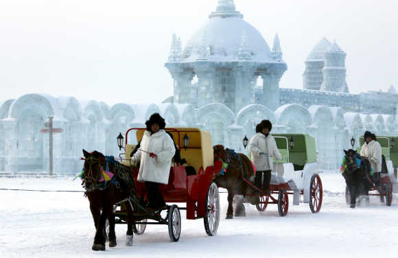 Horse-drawn carriages pass in front of ice sculptures at the 12th Harbin Ice and Snow World display in Harbin, Heilongjiang province, China.