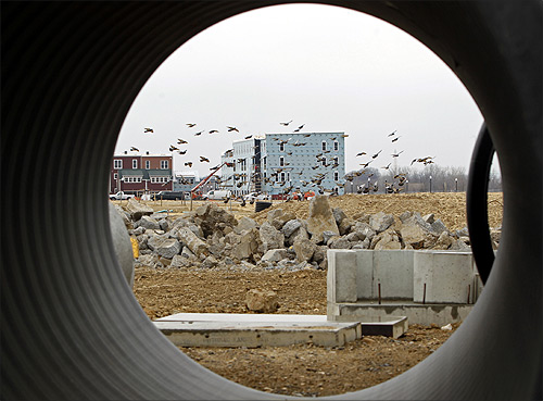 Seen through a water pipe, birds fly across a construction site where new multi-unit buildings are going up in Alexandria, Virginia.