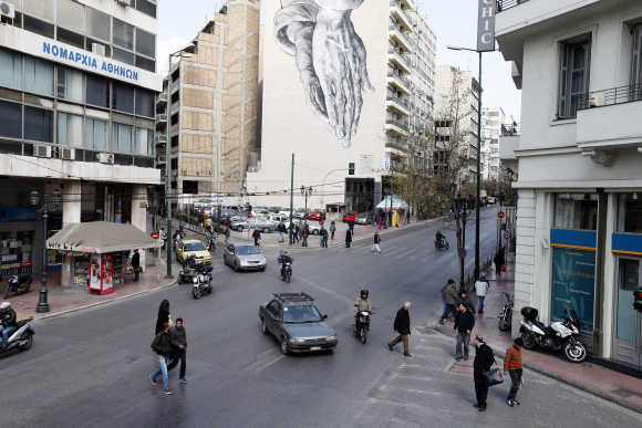 A mural of praying hands is displayed on the side of a hotel in central Athens.