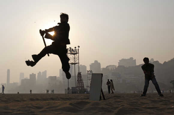 A man jumps in the air to hit a ball as people play cricket by the beach in Mumbai.