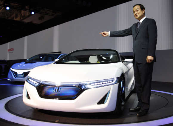 Honda Motor Co President Takanobu Ito poses next to the company's next-generation EV sports car EV-Ster and next-generation plug-in hybrid vehicle AC-X during a news conference at the 42nd Tokyo Motor Show in Tokyo.