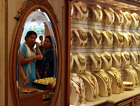 A woman is reflected in a mirror as she tries a gold earring inside a gold jewellery showroom in Kochi.