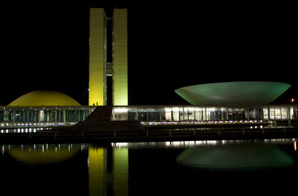 The National Congress building in Brasilia is illuminated with green and yellow lights.