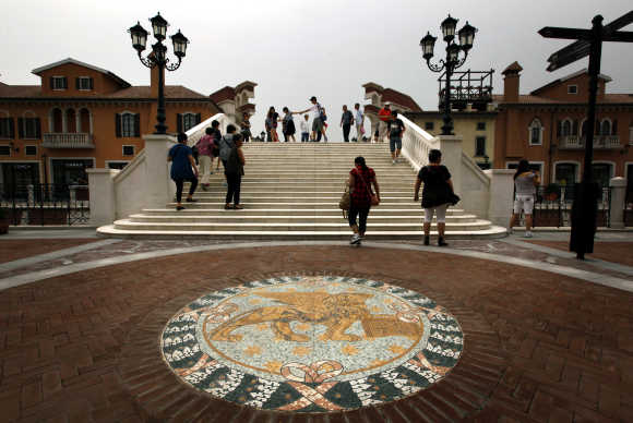 A Venetian Lion emblem adorns the footpath as pedestrians walk across a bridge over a canal that flows through the centre of the Florentia Village in Wuqing, Tianjin, China.