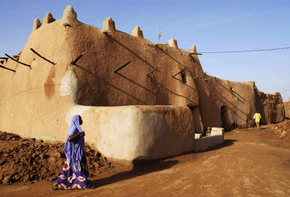A Tuareg woman crosses the street in front of a mud building in the Old Quarter of the desert city of Agadez.
