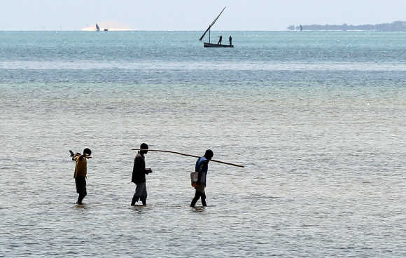 Local fishermen walk to a fishing boat on the Indian Ocean shore line in Vilanculo, Mozambique.