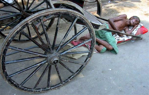A hand rickshaw puller rests on a pavement in Kolkata.