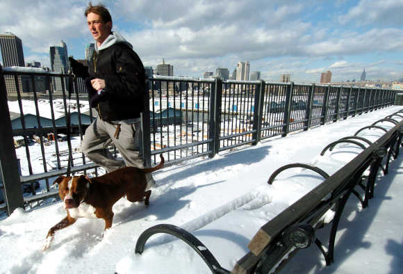 A jogger and his pit bull run along the snow-covered Brooklyn Promenade, across the East River from Manhattan, New York.