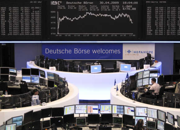 Traders work at their desks in front of the DAX board at the end of the session at Frankfurt stock exchange.