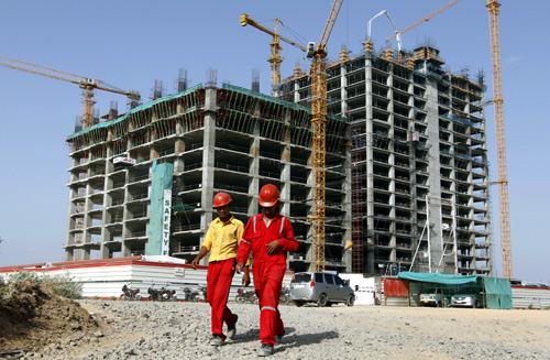 Workers walk in front of a multi-story commercial building under construction on the outskirts of Ahmedabad.