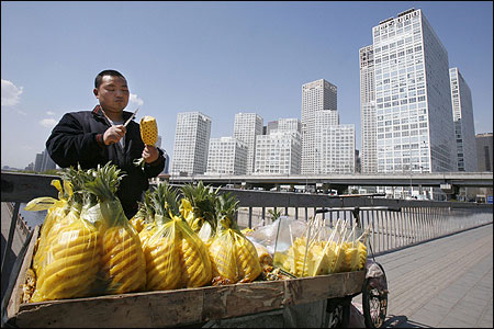 A vendor slices pineapple along the sidewalk in the central business district of Beijing.