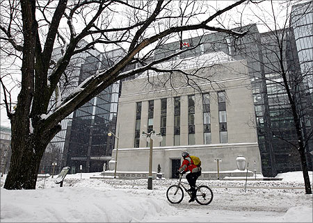 A cyclist passes the Bank of Canada building through a snow covered sidewalk in Ottawa.