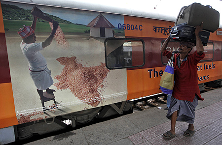 A porter carries luggage of a passenger at a railway station in Kolkata.