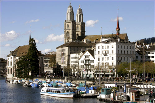 People walk along the Limmat River in front of the Grossmuenster church in the Swiss city of Zurich.
