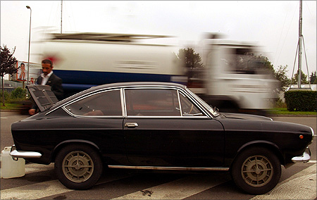 A truck drives by as Marco Santin attempts to fix his Fiat 850 Special which broke down on a roadside in central Milan.