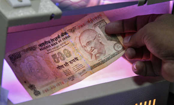 An employee uses an electronic machine to check rupee note inside a bank.