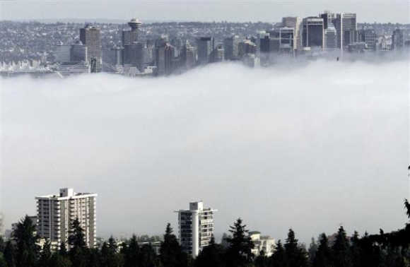 The buildings of downtown Vancouver, Canada, and apartment buildings of the North Shore rise above an afternoon fog over ther harbour.