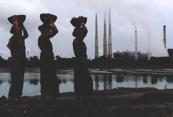 Labourers carry small pieces of coal deposit from liquid ash generated from a thermal power plant (background) in Kolaghat, 75km west of Kolkata.