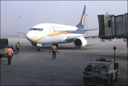 Ground staff guide a Jet Airways aircraft towards a gate on the tarmac at Bengaluru International Airport.