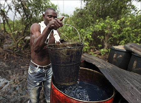 A man collects crude oil from a drum at an illegal refinery in the village of Isuini-biri in Nigeria's Bayelsa state.
