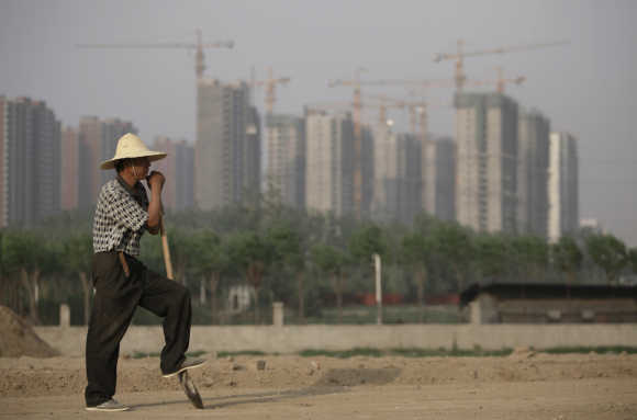 Worker rests on his shovel at a road construction site as cranes are seen in the background at a residential area under construction in Beijing.
