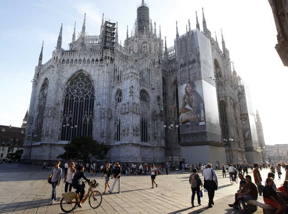 An advertisement is seen on Duomo cathedral as people walk across Duomo square in Milan.