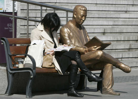 A woman reads a book beside a bronze statue in front of Sejong Centre for the Performing Arts in central Seoul.