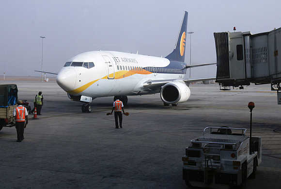 Ground staff guide a Jet Airways aircraft towards a gate on the tarmac at Bangalore International Airport.