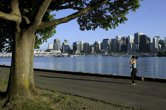 A jogger runs along the seawall in Stanley Park with Vancouver's skyline in the background.
