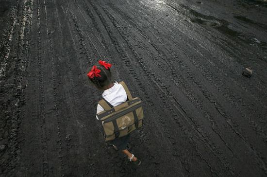 A girl walks on a road covered with oil and soot in an industrial area.