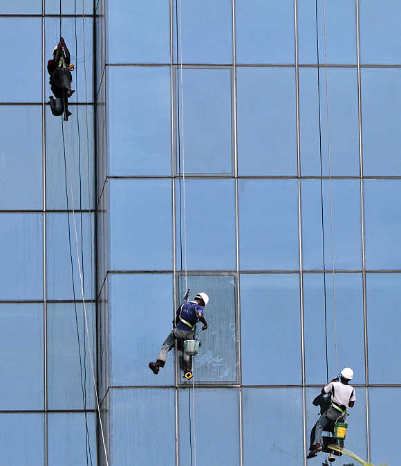 Workers suspended on ropes clean the glass facade of a commercial complex in Chennai,