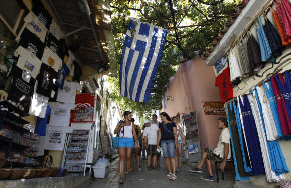 A Greek flag is seen as people walk in an alley at the tourist district of Placka in Athens.