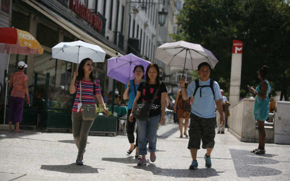 Tourists carry umbrellas as they walk in downtown Lisbon.