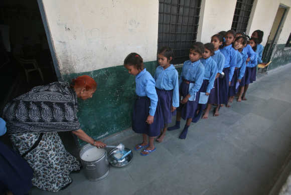 Children stand in line to collect their free mid-day meal distributed by the government inside a primary school in Noida.