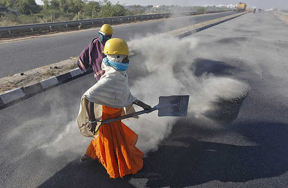 A woman labourer spreads black ash over a road at Raipur village in Gujarat.