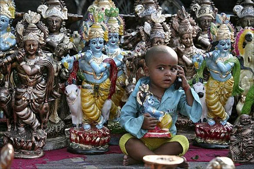 Prem, the son of an idol vendor, plays with a mobile phone in front of the idols of Hindu god Krishna at a roadside on the eve of the Hindu festival of Janmashtami.