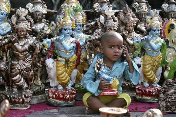 Prem, the son of an idol vendor, plays with a mobile phone in front of the idols of Hindu God Krishna.