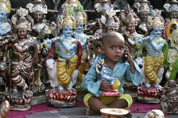 Prem (3), the son of an idol vendor, plays with a mobile phone in front of the idols of Hindu god Krishna.