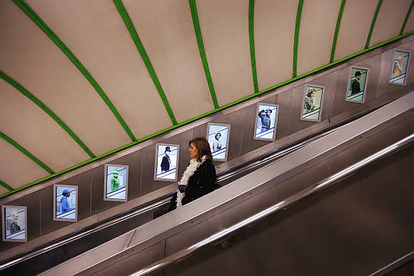A passenger uses the escalator to the platforms at Paddington Underground station, passing posters highlighting London Underground's 150th anniversary.