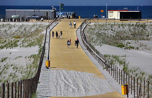 People walk along sand dunes at the Gravenzande coast with the Rotterdam Europort as a backdrop in the Netherlands.
