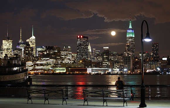 A full moon rises behind the Empire State Building in New York as a man watches along the Hudson River in Hoboken, New Jersey, United States.