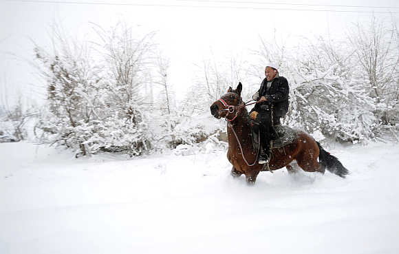 An ethnic Uighur man rides a horse in snow in Yili, Xinjiang Uighur Autonomous Region.