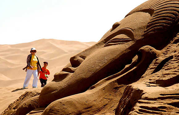 Two tourists look at a sand sculpture in a desert in Turpan in Xinjiang Uygur Autonomous Region.