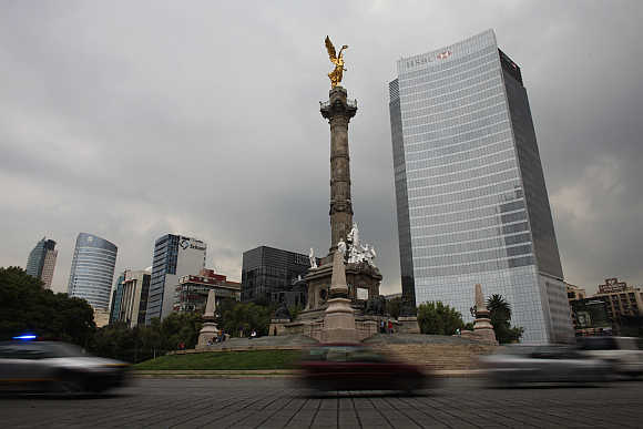 Cars drive past the Angel of Independence monument and British bank HSBC's headquarters in Mexico City.