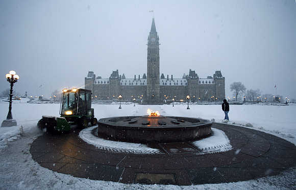 A worker cleans away snow around the Centennial Flame on Parliament Hill in Ottawa, Canada.