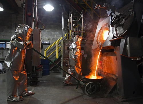 Workers wearing heatproof overalls pour molten gold from a crucible into moulds in a workshop at Kumtor gold mine extraction factory.