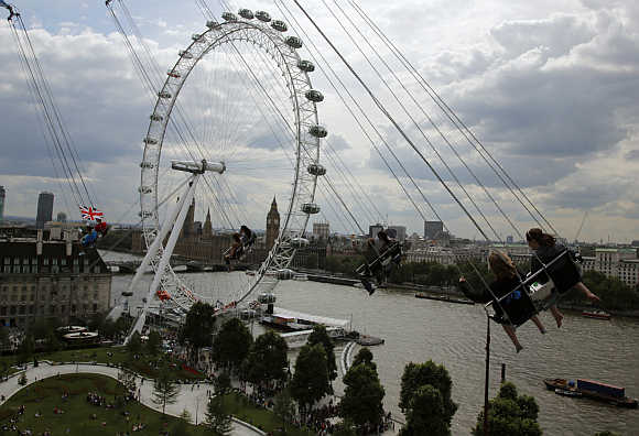 Thrill seekers ride a fairground attraction overlooking the London Eye, left, and Houses of Parliament, right, next to the Thames river in London.