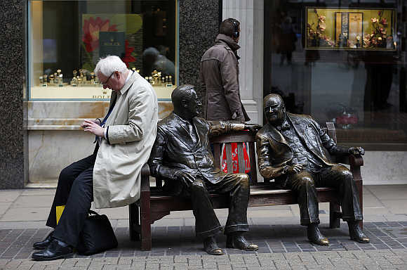 A man looks at his mobile phone while perched on the side of a sculpture entitled 'Allies' by Lawrence Holofcener on New Bond Street in London.